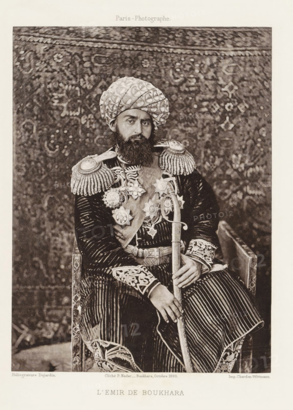 l'Emir de Bukhara, Portrait of the Emir of Bukhara, page, photomechanical print, photographer: Paul Nadar, Bukhara, cliché maker: Dujardin, France, printer (person): Chardon-Wittmann, 1890-10, Paul Nadar, Dujardin, Chardon-Wittmann, photographer, cliché maker, printer (person), Emirate of Bukhara, paper, photoaquatint, height 175 mm x width 132 mm, ruler, sovereign, head-gear: turban, A seated man with a full beard and a patterned turban faces the camera wearing a richly decorated uniform with fringed epaulettes, ornate medals, and embroidered cuffs; he holds a curved sword with both hands across his lap and sits against a tapestry-like patterned backdrop while a carved wooden armrest is visible at his side.