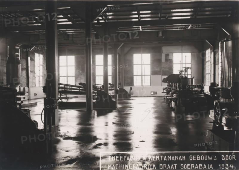 Factory hall, photograph, View into the roller room of the Kertamanah Tea Factory in West Java, built by Machinefabriek Braat in 1934. Part of the binder containing photographs of machines from NV Machinefabriek Braat in Surabaya and Sukabumi intended for the Dutch tea industry in Java and Sumatra, from the period 1931-1937., Java, 1934, photographer, paper, gelatin silver print, height 123 mm x width 172 mm, Person, NV Machinefabriek Braat, workshop-interior, colonial system, tea (leaves), machines, parts of machines, tools and appliances, (non-fruit) products of plants or trees (with NAME), economic history, overseas history, tea culture, business history, Period, 1931 - 1937, A large industrial interior with a polished reflective floor, tall vertical support columns, and a high ceiling with visible beams and skylights; large multi-pane windows along the back and right walls let in bright light that casts reflections on the floor; various heavy machines and mechanical equipment are a...