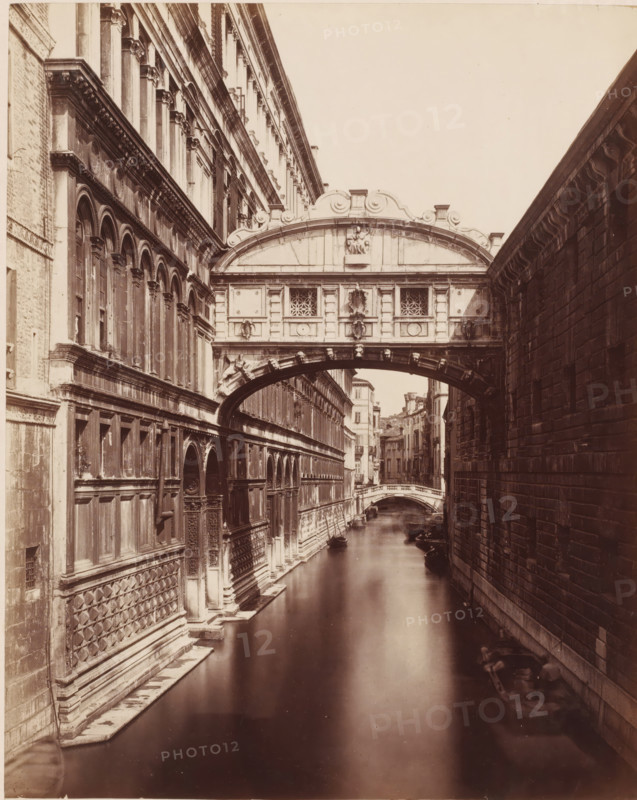 Ponte dei Sospici. (Venezia), View of the Bridge of Sighs in Venice, Italy, photograph, number: '3519.', collector's mark: 'RIJKS SCHOOL FOR ARTS HANDBOOK, GROUP', inscription: 'Burg der Zuchten', inscription: 'I', photographer: attributed to Giorgio Sommer, Venice, 1857 - 1914, Giorgio Sommer, photographer, Attributed to, pasteboard, paper, albumen print, height 478 mm x width 318 mm, landscape with bridge, viaduct or aqueduct, canals, waters (in city), Ponte dei Sospiri, A narrow canal runs between two tall stone buildings with an ornate covered bridge spanning across the water; the left building has rows of arched windows, decorative columns, and patterned stonework along its lower face while the right building shows large rectangular blocks and a plain facade; the bridge features sculpted reliefs, carved details, and small decorative windows above an arched passage; beyond the bridge the canal continues past additional buildings and a smaller arched bridge, and several small boats ...