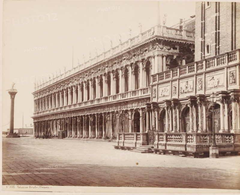 Palazzo Reale. (Venezia), View of the Piazzetta and Palazzo Reale where the Libreria Vecchia is housed, Venice, Italy, photograph, number: 'No. 3511.', inscription: 'II', number: '39', inscription: 'Library in Venice (...)', collector's mark: 'RICH SCHOOL FOR ART HANDBOOK, GROEP', photographer: attributed to Giorgio Sommer, 1857 - 1914, Giorgio Sommer, photographer, Attributed to, pasteboard, paper, albumen print, height 319 mm x width 479 mm, study, 'studiolo', library, square, circus, hôtel, ie small palace in city, Piazzetta, A long ornate stone building with a colonnaded facade and arched openings runs across the image, its upper balustrade lined with standing statues and decorative relief panels, while the lower level shows detailed columns, sculpted doorways, and carved stonework; a tall column topped with a statue stands in the open paved square to the left, and lamp posts and benches are visible along the building, with a large open paved foreground extending toward the viewer.