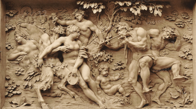 Hautrelief from Elfenbein, ein Bacchanale v. J. Elhafen. 1708, Ivory relief depicting a bacchanal, by Ignaz Elhafen, photomechanical print, number: 'Blatt 190.', Germany, cliché maker: anonymous, after sculpture by Ignaz Elhafen, printer (person): attributed to Johann Baptist Obernetter, Munich, 1869 - 1887, Ignaz Elhafen, photographer, after sculpture by, printer (person), Bavaria, Attributed to, pasteboard, paper, collotype, photoprint, height 128 mm x width 216 mm, height 415 mm x width 539 mm, piece of sculpture, reproduction of a piece of sculpture, bacchanal: Bacchus with his wine-flushed train (thiasos), A carved relief panel in a warm stone tone shows multiple partially and fully nude human figures intertwined among carved foliage and trees, with some figures wearing wreaths of leaves and one holding a cluster of grapes; a central seated female figure holds a hand near her chest and grasps a round shallow object, while a muscular male figure to the right plays a double pipe and...