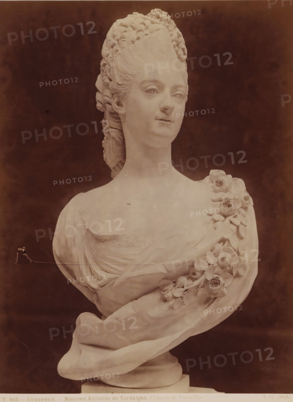 Bust of Adélaïde de Sardaigne, by A. Coysevox, Coyzevox - Madame Adélaïde de Sadaigne. Château de Versailles., photograph, inscription: 'pl 19', name: 'A. GIRAUDON EDITOR 15. R. BONAPARTE. PARIS', number: 'T 465', photographer: Adolphe Giraudon, Paris, c. 1875 - c. 1900, paper, pasteboard, albumen print, height 255 mm x width 191 mm, sculpture, historical persons - BB - woman ((full) bust portrait), A marble bust of a woman shown from the chest upward against a dark background, featuring an elaborate high coiffure with carved curls, a smooth face with neutral expression and detailed eyes and mouth, a draped garment across the shoulders with sculpted lace along the neckline, and a garland of carved roses and leaves draped over one shoulder, all mounted on a round pedestal.