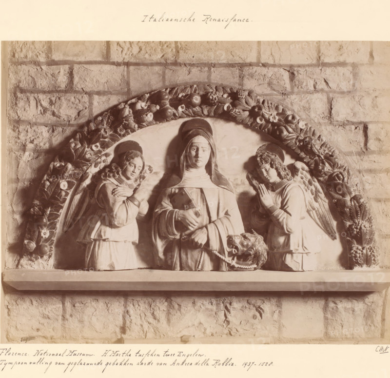Tympanum addition depicting Martha between two angels by Andrea della Robbia, Florence. National Museum. St. Martha between two Angels., photograph, inscription: 'Italian Renaissance.', inscription: 'CWN.', collector's mark: 'KUNSTNIJVERHEIDSCHOOL QUELLINUS AMSTERDAM FRANS HALSSTRAAT 14.', collector's mark: 'INSTITUUT VOOR KUNST-NIJVERHEIDSONDERWIJS GABRIËL METSUSTRAAT No. 16 AMSTERDAM', Europe, c. 1875 - c. 1900, photographer, paper, pasteboard, albumen print, albumendruk, height 189 mm x width 245 mm, angels, the patroness of housewives, Martha of Bethany, possible attributes: aspergillum, broom, bunch of keys, dragon, ladle, sculpture (relief, sculpture), A stone relief set against a textured brick wall depicting a central robed figure with a covered head and a calm facial expression flanked by two winged figures in robes, each with folded hands and downward gazes, all within a semicircular frame decorated with carved fruits and flowers, a lion head with an open mouth holding a rope...