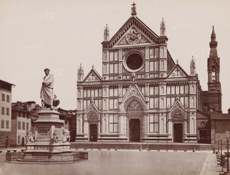 Chiesa di S. Croce e statua di Dante, View of Santa Croce and the statue of Dante in Florence, Italy, Firenze, photograph, inscription: 'Brogi', number: '3033.', number: '11', photographer: Giacomo Brogi (possibly), Florence, publisher: attributed to Edizioni Brogi, after sculpture by Enrico Pazzi, 1865 - 1881, Enrico Pazzi, after sculpture by, Tuscany, Attributed to, pasteboard, paper, albumen print, albumendruk, height 317 mm x width 445 mm, Person, Dante Alighieri, historical persons, monument, statue, church (exterior), Santa Croce, A large ornate stone façade of a church fills the center and right of the image, featuring rectangular panels, decorative arches, a circular window, peaked gables with carved details, sculpted reliefs above doorways, and tall pointed spires. In front of the church to the left stands a tall statue of a robed figure on a multi-tiered pedestal surrounded by a low metal fence; the pedestal is flanked by sculpted lion figures and additional carved ornamentat...