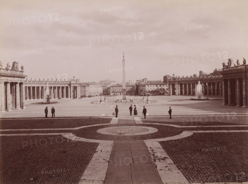 Piazza di S. Pietro, vista d, View of St. Peter's Square in Vatican City, Italy, Roma, photograph, number: '8472.', number: '95', photographer: Carlo Brogi (possibly), Vatican City, publisher: attributed to Edizioni Brogi, Florence, 1881 - 1900, Carlo Brogi, Edizioni Brogi, photographer, publisher, Tuscany, Attributed to, pasteboard, paper, albumen print, height 317 mm x width 445 mm, square, circus, St. Peter's Square, A wide open plaza with a central obelisk flanked by two long colonnades topped with statues and balustrades, fountains with jets of water at each side near the colonnades, paved ground with concentric circular stone patterns in the foreground, several small groups of people standing and walking across the plaza dressed in dark coats and hats, low buildings and rooftops visible beyond the obelisk, and a sky filled with light clouds above.