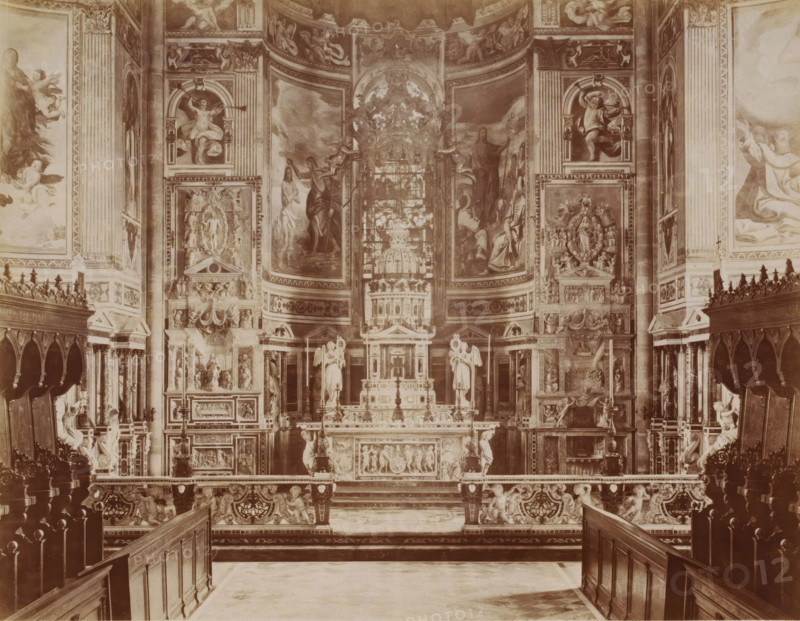 Interior of the monastery church Certosa di Pavia, seen towards the choir, Pavia, Italy, Coro dela Chiesa, Certosa di Pavia, photograph, collector's mark: 'VOSMAER', number: '4633.', photographer: attributed to Giacomo Brogi, Pavia (city), publisher: attributed to Giacomo Brogi, 1856 - 1881, Giacomo Brogi, photographer, publisher, Lombardy, Attributed to, pasteboard, paper, albumen print, height 316 mm x width 421 mm, abbey, monastery, convent, Roman Catholic church, parts of church interior, A sepia-toned wide interior view of an ornate chapel or church altar area with carved wooden pews and choir stalls in the foreground leading toward a raised altar decorated with sculpted figures and relief panels. The central altar structure features statues of angels and saints flanked by tall columns and intricately carved panels, with a domed architectural element and a framed stained-glass or painted panel behind it. The walls and curved apse are covered with large frescoes or paintings depict...