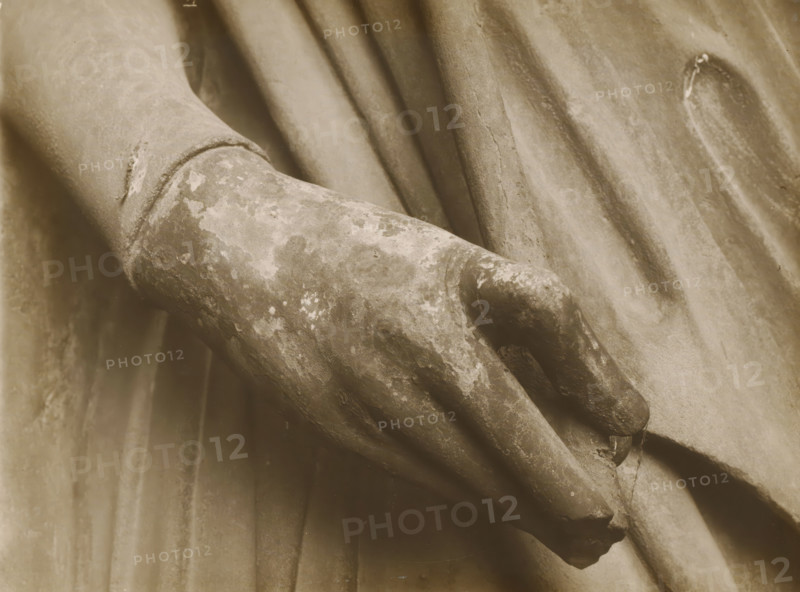Adamspforte (r.Hand), Detail of the Adamspforte in Bamberg Cathedral, album page, photograph, This photo is part of an album., number: '47.', Bamberg, 1900 - c. 1920, photographer, Bavaria, paper, baryta paper, gelatin silver print, developed gelatin silver print, height 227 mm x width 168 mm, church (exterior), Bamberg Cathedral, A close-up sepia-toned view of a weathered stone hand resting against draped fabric, showing textured surface wear and flaking, with visible folds and creases in the surrounding cloth.