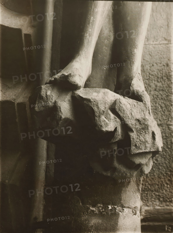 Detail of the Adamspforte in the cathedral of Bamberg, Adamspforte, Eva, Sockel, album page, photograph, This photo is part of an album., number: '59', inscription: 'Kunsthist. Seminar, Marburg (Lahn), Photogr. Abteilung, Vervielfältigung, untersagt.', Bamberg, 1900 - c. 1920, photographer, Bavaria, paper, baryta paper, gelatin silver print, developing gelatin silver print, height 239 mm x width 178 mm, church (exterior), Bamberg Cathedral, A close-up black-and-white photograph of two stone feet resting on a rough textured rock surface, showing worn and chipped edges and visible surface irregularities; the lower legs extend upward with smooth but weathered contours, and surrounding background areas include vertical stone columns and a rock wall with coarse masonry, all rendered in soft contrasts of light and shadow.