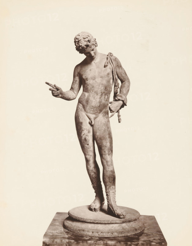 Sculpture of Narcissus, Museo di Napoli Narciso, album page, photograph, This photo is part of an album., number: '1535', workshop stamp: 'Giorgio Sommer, Largo Vittoria, Napoli', photographer: Giorgio Sommer, Naples, 1874 - in or before 1879, paper, albumen print, height 249 mm x width 201 mm, sculpture, (story of) Narcissus, A grayscale photograph of a full-length classical statue of a nude male figure standing on a round stepped pedestal, the figure leaning slightly with weight on one leg, curly hair, head tilted downward, left arm bent with hand pointing outward, right arm resting at the side holding a draped cloth or sash that falls over the shoulder, visible detailed musculature and worn surface texture, one foot bare and the other wearing a laced sandal, the background plain and light.