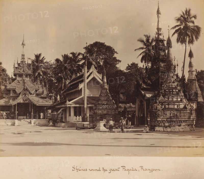 Shrine around the Shwedagon Pagoda, Yangon, Myanmar, album page, photograph, Pagoda with burial chambers and palm trees, taken from an open area. The country has officially been called the Union of Myanmar since 1989; before that, it was called Burma. Since November 7, 2005, the capital has officially been the centrally located Naypyidaw (near Pyinmana), although the relocation only began on that date. The former capital is Rangoon (Yangon), the largest city in the country., caption: 'Shrines round the great Pagoda, Rangoon', c. 1880 - c. 1900, photographer, paper, pasteboard, albumen print, height 206 mm, width 268 mm x width 301 mm, height 380 mm, A wide sepia photograph showing ornate temple buildings and stupas with tiered, carved roofs and spires, surrounded by tall palm trees and dense foliage, with a large open paved area in the foreground and a few people standing and sitting near the base of one of the stupas.