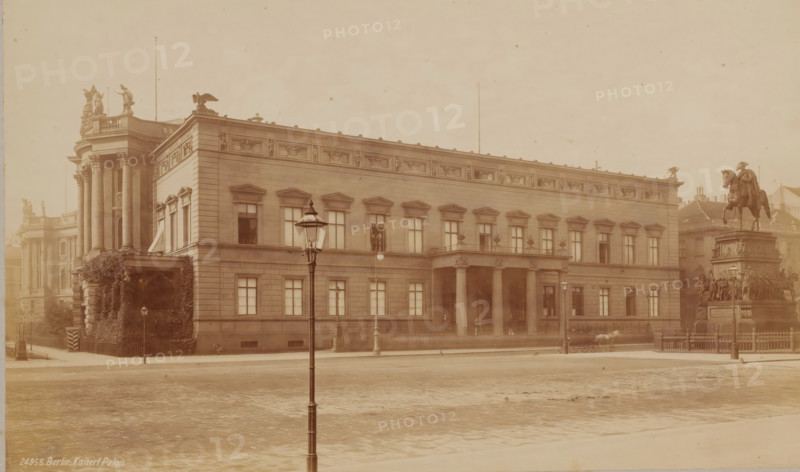Kaiserlicher Palast, Berlin, Germany, photograph, Germany., check stamp: 'Frith's ...', inscription: '24955. Berlin, Kaiserl Palais.', inscription: 'Frith's', photographer: Francis Frith & Co., c. 1875 - c. 1900, paper, pasteboard, albumen print, height 158 mm, width 261 mm x width 370 mm, height 316 mm, A wide stone building with a decorated cornice and rows of tall windows occupies the center of the scene, featuring a columned portico at its entrance and sculptural reliefs along the upper frieze; a large equestrian statue on a multi-tiered pedestal stands to the right, surrounded by smaller sculpted figures and a low metal fence; ornate street lamps line the cobblestone street in front of the building, and a solitary lamppost is prominent in the foreground; architectural details include pedimented window surrounds, pilasters, and a rounded corner section with tall columns and statues on the roof; a carriage and horse are visible near the statue, and nearby buildings can be seen behin...