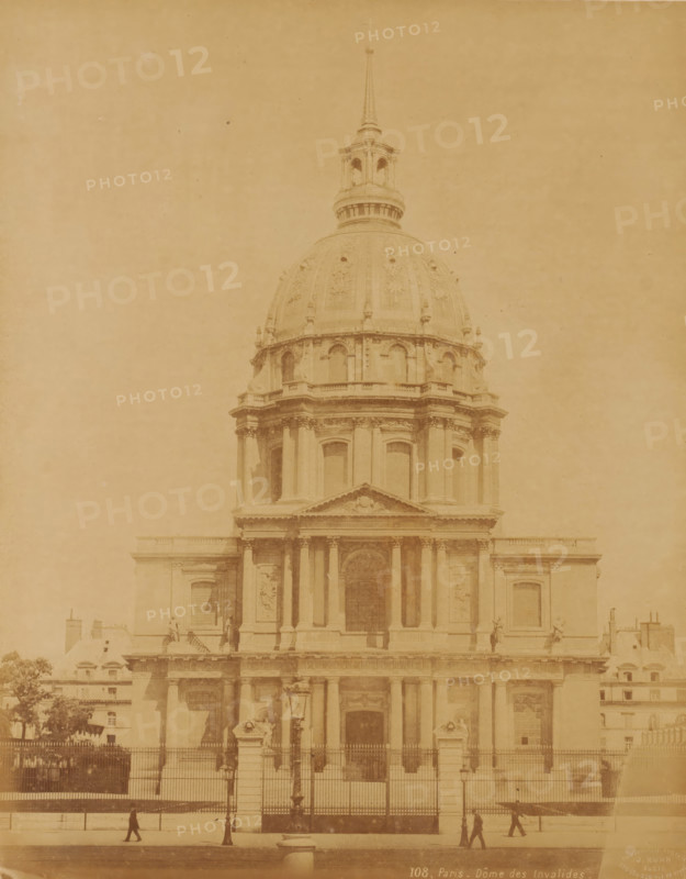 Hôtel National des Invalides ('Dôme des Invalides'), Paris, France, photograph, Frontal view of the Hôtel National des Invalides, located in the 7th arrondissement of Paris. It was founded in 1671 by Louis XIV., inscription: '108, Paris - Dôme des Invalides', check stamp: 'Photographic Company, J. Kühn, 220 170174 Rue de Rivoli', number: '16.', publisher: J. Kühn (publisher), c. 1885 - c. 1910, paper, pasteboard, albumen print, height 275 mm, width 218 mm x width 447 mm, height 326 mm, Dôme des Invalides, A large classical building facade with a tall ornate dome and a spire rising above it, featuring columns, arches, sculpted reliefs, and decorative balustrades, a fenced forecourt with stone pillars and lamp posts in front, several small human figures walking along the pavement, and portions of adjacent lower buildings and trees visible at the edges.