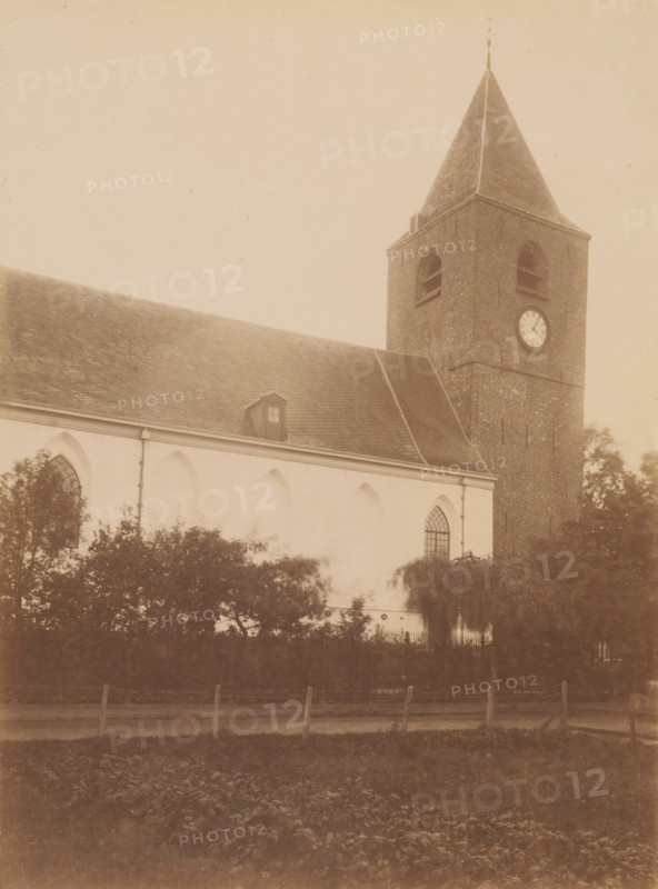 View of the St. Mary's Church in Buitenpost, photograph, annotation: 'Buitenpost, Dutch Reformed Church, Achtkarspelen, I. 278 No. 1401', Buitenpost, photographer: AJM Mulder (possibly), c. 1890 - c. 1910, AJM Mulder, photographer, Attributed to, paper, pasteboard, albumen print, height 224 mm x width 168 mm, church (exterior), A sepia-toned photograph of a church exterior showing a sloped roof with a small dormer window and a tall brick tower with a pointed roof and a circular clock face, arched windows along the whitewashed wall, trees and shrubbery in front of the building, and a low fence along the foreground.