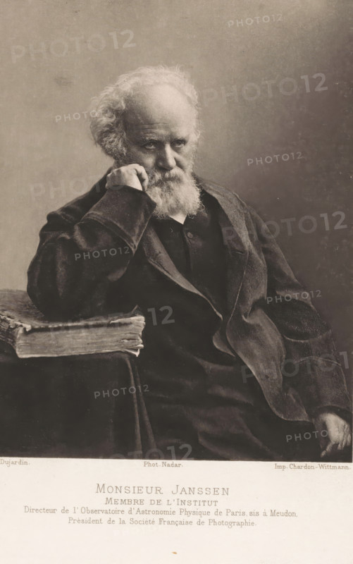 Monsieur Janssen, Portrait of Pierre Janssen, page, photomechanical print, inscription: 'Membre de l'Institut Telefoon de l'Observatoire d'Astronomie Physique de Paris sis à Meudon, Prèsident de la Sociéte' Française de Photographie.', photographer: Félix Nadar, Paris, cliché maker: Dujardin, printer (person): Chardon-Wittmann, c. 1882 - in or before 1892, printer (person), paper, photoaquatint, height 142 mm x width 115 mm, Person, Pierre Jules César Janssen, astronomy (and cosmography), An elderly man with a full white beard and mustache sits leaning his head on his hand, his fingers touching his cheek, wearing a dark coat and jacket with visible folds and textured fabric, his gaze directed slightly downward, beside him a thick, worn book rests on a surface draped with cloth, the background is plain and softly shaded.
