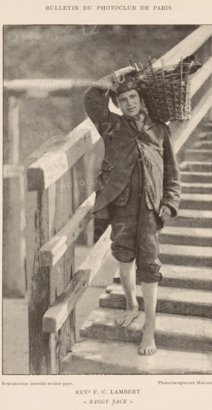 Boy with a basket on his shoulder walking down a staircase, Raggy Jack, page, photomechanical print, inscription: 'Bulletin du Photoclub de Paris', inscription: 'Reproduction interdite en tous pays.', photographer: FC Lambert, cliché maker: Jean Malvaux, c. 1888 - in or before 1893, paper, autotypie, height 180 mm x width 108 mm, youth, adolescent, carrying something in basket, bag, rucksack, flight of steps, A sepia-toned photograph showing a barefoot young man standing on wooden steps beside a railing, wearing rolled-up trousers and a worn jacket, with a patterned scarf around his neck and a cap on his head, holding a woven basket balanced on his shoulder while one hand rests on his head and the other hangs by his side, with the wooden railing and steps forming strong diagonal lines in the composition.