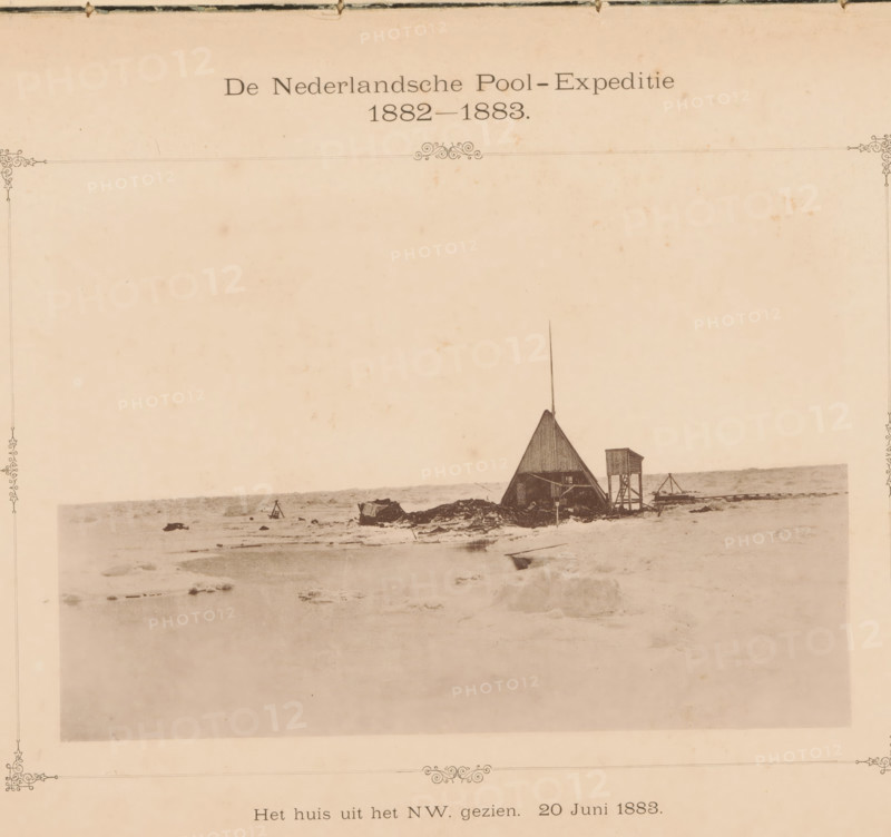 View of a house on the Kara Sea, The house from the NW. seen. June 20, 1883., page, photomechanical print, inscription: 'The Dutch Polar Expedition 1882-1883', photographer: H. Ekama, Karskoye More, cliché maker: E. Diener, Glauchau, c. 1881 - in or before 1886, Saxony, paper, collotype, photoprint, height 131 mm x width 206 mm, landscapes in polar regions, icefield, A mostly empty pale sheet with a faint decorative border contains a small sepia photograph near the top center showing a flat icy landscape with a triangular tent-like structure topped by a tall slender pole and an adjacent raised wooden platform on stilts, scattered debris and small items around them, and a distant horizon line; the surrounding paper shows light spots and aging marks.