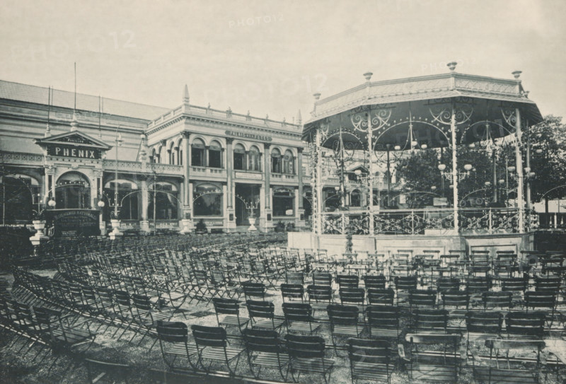 Pailas des fêtes, View of a kiosk in front of Palais des fêtes during the 1894 World Exhibition in Antwerp, photomechanical print, Part of a cover with 49 plates., inscription: 'Exposition Universelle D'Anvers 1894', photographer: Charles Bernhoeft, Antwerp, cliché maker: Charles Bernhoeft, Luxembourg (city), c. 1894, Charles Bernhoeft, photographer, cliché maker, printer (person), paper, collotype, photoprint, height 154 mm x width 222 mm, civic architecture, edifices, dwellings, world fair, world exhibition, World Exhibition 1894 (Antwerp), Period, 1894, A large outdoor scene showing rows of folding chairs arranged across a paved area in front of an ornate raised bandstand with decorative railings, arched supports, and hanging globe lamps, positioned to the right; to the left and center is a two-story classical building with arched windows, columns, ornamental cornices, and a pavilion entrance topped by a triangular pediment; lamp posts and decorative streetlights are visible near th...