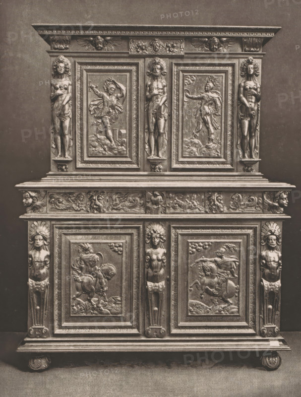 16th century French wooden cabinet, at the 1877 Exposition Rétrospective in Lyon, France, page, photomechanical print, inscription: 'EXPOSITION RÉTROSPECTIVE DE LYON, PAR JB GIRAUD.', number: 'PL. XLII.', inscription: 'ARMOIRE, FRANCE_XVIe SIÈCLE, COLLECTION DE Mme Vve DARDEL.', Lyon, cliché maker: Dujardin, printer (person): Imprimerie Eudes, Paris, 1877 - in or before 1880, photographer, printer (person), paper, photoaquatint, height 252 mm x width 191 mm, ornamental cupboard (wood and other phytogenic material), A tall carved wooden cabinet with ornate panels and sculpted figures, shown straight-on against a plain background, featuring a top cornice with decorative molding and small winged faces, a central section with three framed relief panels depicting human figures in dynamic poses and vertical carved caryatid-like figures flanking the panels, a middle frieze with assorted carved motifs and small faces, and lower doors with framed relief scenes showing mounted figures and flowin...