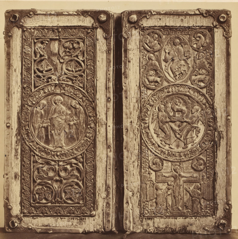 Ivory diptych with depictions from the New Testament, from the Cathedral of Our Lady in Tournai, displayed at an exhibition of religious objects from the Middle Ages and Renaissance in 1864 in Mechelen, photograph, page, number: '4', photographer: Joseph Maes, Mechelen, 1864, paper, albumen print, height 198 mm x width 199 mm, New Testament, piece of sculpture, reproduction of a piece of sculpture (bone, ivory, arts), Period, A close-up view of two adjacent carved wooden panels with metal corner brackets and hinge between them, each panel featuring circular medallions with relief figures and ornate foliage motifs, framed by carved borders and vertical wood grain, with visible wear and small round rivets along the edges.