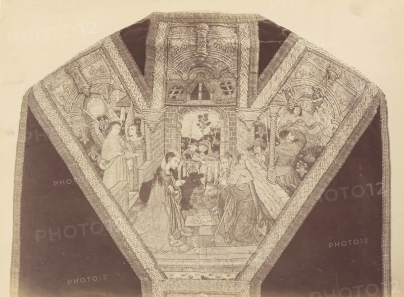 Chasuble from a church in Lier, displayed at an exhibition on religious objects from the Middle Ages and Renaissance in 1864 in Mechelen, photograph, page, number: '13', photographer: Joseph Maes, Mechelen, 1864, paper, albumen print, height 194 mm x width 258 mm, chasuble, Period, A triangular textile panel with ornate embroidered borders surrounds a central scene showing figures inside an arched architectural interior; two kneeling figures face each other near a small enclosed manger while a seated figure and a standing figure with a staff are nearby, and additional standing figures and angels appear along the sides; the embroidered architecture includes columns, arches, a tiled floor, and a window revealing a landscape with trees and distant buildings; patterned woven trims frame the scene and extend outward against a dark background on either side.