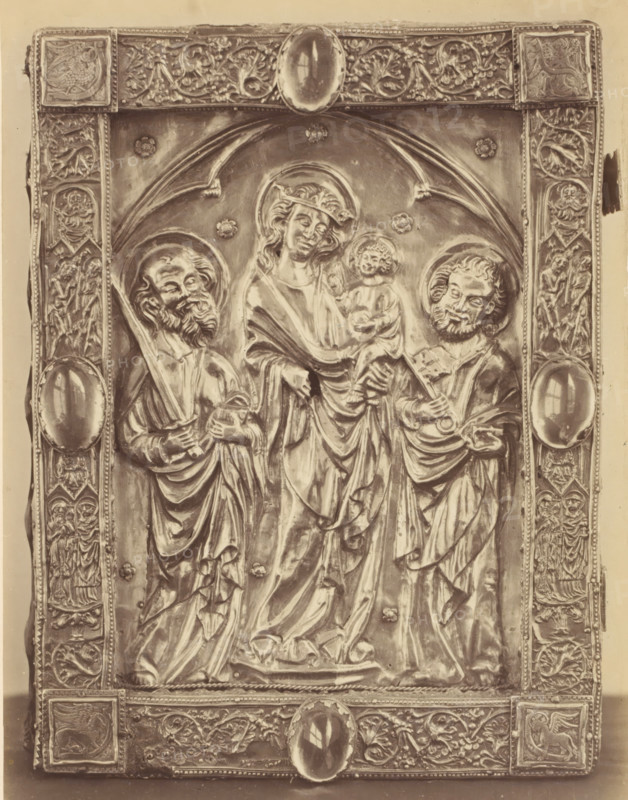Book binding with Mary and Child and Peter and Paul from the Basilica of Our Lady in Tongeren, displayed at an exhibition on religious objects from the Middle Ages and Renaissance in 1864 in Mechelen, photograph, page, number: '15', photographer: Joseph Maes, Mechelen, 1864, paper, albumen print, height 240 mm x width 185 mm, book-cover, binding, Mary standing (or half-length), the Christ-child sitting on her arm (Christ-child to Mary's left), Period, A rectangular metal relief panel with an ornate border showing floral and figured decorative motifs surrounds a central scene of three robed figures under an arched framing element; the central figure wears a halo and holds a small seated child, while the two flanking figures also wear halos and hold objects in their hands; the border contains oval cabochon-like elements and numerous small carved scenes and vegetal patterns, and the surface displays highlights and shadows that accentuate folds in the drapery and facial features.