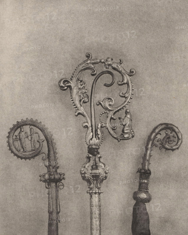 Three decorated episcopal staffs, displayed at an exhibition of religious objects from the Middle Ages and Renaissance in 1864 in Mechelen, page, photomechanical print, number: '-42', number: '1. 2. 3', number: '3 - 1 - 2', photographer: Joseph Maes, Mechelen, clichémaker: Simonau & Toovey, Antwerp, 1864 - in or before 1866, paper, photolithography, height 224 mm x width 180 mm, (liturgical) equipment of church, Period, 1864, Three ornate crook-shaped objects with decorative scrolls are shown against a plain background, each featuring carved embellishments and curved tops. The central piece is the largest with an elaborate swirling design, bead-like edging, floral motifs, and a small figurine integrated into the scrollwork; its shaft has carved ornamentation and a detailed base. The left piece has a rounded curled top with a framed scene incorporated into the curl and a shaft with a rounded, studded collar. The right piece has a narrower curled top with foliate carving, a banded shaft,...