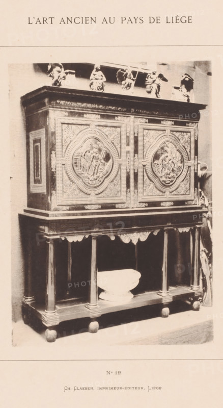 Wooden cabinet, installed in the archaeological museum in Liège, Belgium, L'Art Ancien au Pays de Liége, photomechanical print, This print is part of a cover with twenty prints, a title page and a list of images., number: 'No 12', Liège, printer (person): Ch. Claesen Éditeur, publisher: Ch. Claesen Editeur, c. 1879 - in or before 1884, Ch. Claesen Éditeur, printer (person), publisher, paper, collotype, photoprint, height 228 mm x width 162 mm, permanent exhibition, museum, ornamental cupboard (wood and other phytogenic material), A tall ornate wooden cabinet stands on a lower open shelf supported by turned columns and rounded feet, the cabinet doors decorated with large circular relief panels surrounded by intricate carved floral and geometric patterns, a wide cornice with decorative molding tops the piece, small sculpted figures and statuettes are arranged along the top edge, a shallow bowl rests on the lower shelf between the columns, the photograph shows the furniture against a plai...