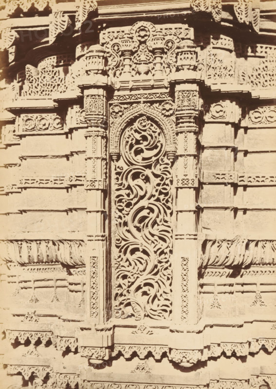 Decoration on the base of a minaret of the Rani Rupamati Mosque in Ahmedabad, The Queen's Mosque in Mirzapoor.- Niche in lower part of base of Northern Minaret, photograph, page, number: '32.', photographer: Thomas Biggs, Ahmedabad (city), c. 1856 - in or before 1866, Thomas Biggs, photographer, Gujarat, paper, albumen print, height 189 mm x width 136 mm, temple, shrine, Islam, Mohammedanism, base (, column, pillar), ornamenting, decorating, applied arts, Rani Rupamati Mosque, A close-up of a carved stone facade showing an ornate vertical panel with swirling, organic openwork patterns framed by carved pilasters, flanked by horizontal bands and rectangular blocks with repetitive carved motifs, rosettes, and decorative borders, with layered cornices and small projecting brackets topped by a carved entablature and additional lattice-like panels.