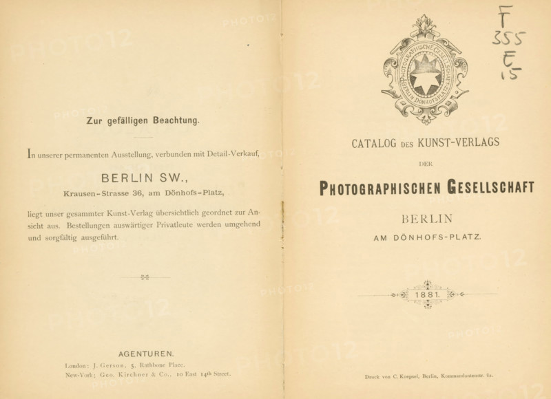 Catalog des Kunstverlags der Photographischen Gesellschaft Berlin 1881, book, name: 'Henri Hymans, Bruxelles', writer (clerical worker): various manufacturers, printer (person): C. Koepsel, Berlin, 1881, writer (clerical worker), printer (person), paper, albumen print, height 191 mm x width 130 mm x thickness 10 mm, The image shows an open two-page spread of an old printed catalog with a vertical fold down the center and aged beige paper; the right page features an ornate circular emblem near the top with decorative flourishes and a central star-like shape, while both pages display multiple lines of printed layout elements and ornamental horizontal dividers; there are small stains and spots on the paper and a handwritten pencil annotation near the top right edge, and the overall appearance includes slight discoloration and wear along the center fold and edges.