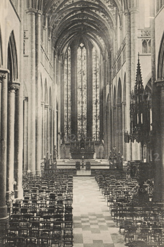 Huy. - La Collégiale, Interior of the Collegiate Church of Our Lady and Domitian of Huy, page, photomechanical print, photographer: attributed to Victor Gaillard, Huy, cliché maker: attributed to Emile Aubry, Brussels, c. 1885 - in or before 1890, Hoei, Attributed to, paper, collotype, photoprint, height 158 mm x width 105 mm, interior of church, A long interior view of a vaulted stone building with tall ribbed arches and a high stained glass window at the far end, a central aisle with a checkered floor leading toward an altar area, rows of wooden chairs arranged on either side of the aisle, tall cylindrical columns with carved capitals lining both sides, ornate carved stone and metalwork visible along the right side including a dark, pinnacled structure, and soft light filtering through the large vertical window panels.