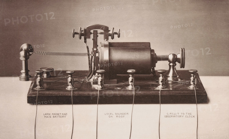 View of the mechanism of the Boston Time-Ball, Massachusetts, Boston Time-Ball, page, photomechanical print, number: 'Plate No. 3.', Boston (Massachusetts), cliché maker: Heliotype Printing Company, c. 1876 - in or before 1881, photographer, North America, paper, collotype, photogravure, height 145 mm x width 234 mm, Print on sixth unnumbered page after page 31., mechanics, (instruments for) measurement of time, A sepia-toned photograph of an antique electrical apparatus mounted on a wooden base, showing cylindrical and rounded metal components, threaded knobs, binding posts, and exposed coiled springs, with several thin wires connecting terminals and looping across the base; the device includes a prominent central cylinder, adjustable screw mechanisms with knurled wheels, upright rounded supports at one end, and clusters of small metal fittings and insulated wire wrappings visible along the connections.