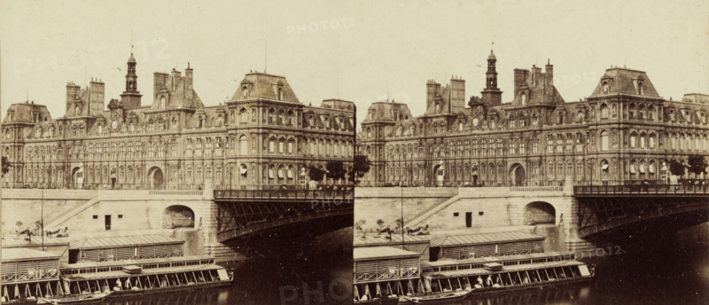 City Hall of Paris seen across the Seine, stereograph, inscription: 'Banselin optician Ft. 14. R. de Seine. Paris.', Paris, c. 1860 - c. 1880, photographer, pasteboard, paper, albumen print, albumendruk, height 84 mm x width 175 mm, townhall, Stadhuis (Paris), A sepia-toned photographic view showing a long ornate stone building with mansard roofs, dormer windows, decorative cornices, and tall chimneys, stretching across the riverside. In front of the building is a stone embankment with an arched bridge opening and a metal-trussed bridge span extending over dark water. Lower on the river are covered wooden platforms and long narrow boats moored alongside, some with awnings and visible seating. Trees and small lampposts dot the embankment, and the sky above is pale and empty.