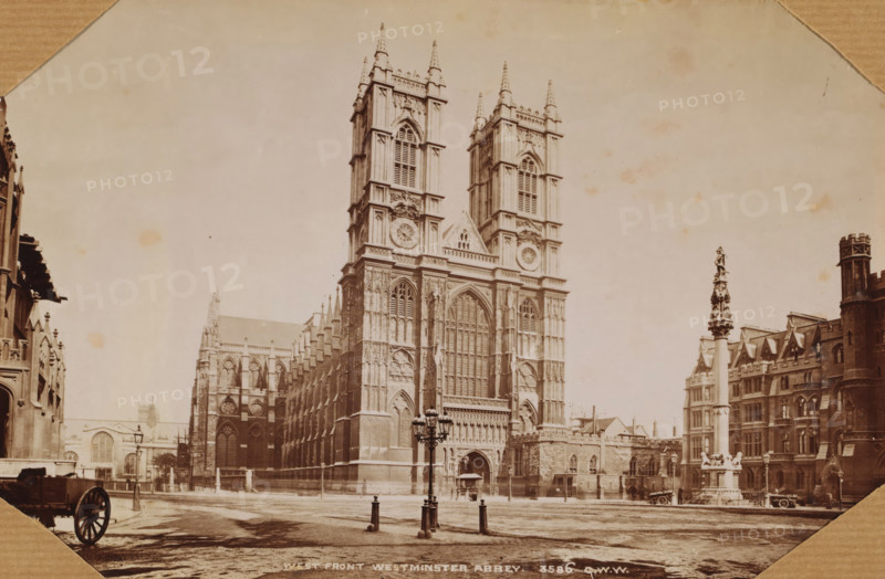 London. Westminster Abbey, photograph, 1850 - 1900, photographer, paper, albumen print, height 130 mm x width 180 mm, height 300 mm x width 250 mm, London, Westminster Abbey, A sepia-toned photograph of a large Gothic cathedral with two tall, ornate towers flanking a central arched entrance, detailed stone tracery and large arched windows, and decorative sculptural elements on the façade; a paved open area in front with a decorative lamppost and short posts with chains; to the right a tall column topped with a statue situated before a row of stone buildings with gabled roofs and a round turret; to the left additional stone buildings and architectural details and a partial view of a carriage wheel in a corner; the sky above is pale and the image has a worn, aged appearance.