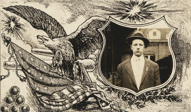 Photo portrait of a young man framed by a drawn representation of an eagle, an American flag, a cannon and cannonballs, postcard, inscription: 'ELMER JACQUES, GOV, KV., PHOTOGRAPHER', photographer: Elmer Jacques, United States of America, in or after 1907 - c. 1930, North America, paper, gelatin silver print, gelatin silver developing print, height 100 mm x width 150 mm, A sepia-toned collage shows a drawn eagle with outstretched wings and an open beak on the left, clutching a striped and starred cloth draped over stacked cylindrical shapes and surrounded by decorative foliage and round cannonball-like spheres, while on the right a framed oval portrait of a young man wearing a dark hat, a suit jacket, and a high-collared shirt is set against a background of a building facade and a doorway.