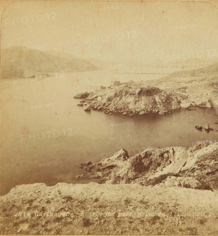 Cartagena. Entrance to the port, prise de Trinca Botijas, View of the entrance to the port of Cartagena, Spain, Views and landscapes in Europe, Africa and Asia, Geographical Sculpture Gallery, collected by MJ Broekhuijsen, Head of a school in Amsterdam, stereograph, Bottom left of photo numbered: 2814., annotation: 'Cartagena, great naval port, one of the best ports of the Mediterranean., The city lies entirely in the background, a good half hour away from us. At the entrance to the port, on the left on a 300 M. high hill, the Château de Galeras, on the right flat, by the sea, the Fort St. Anna, both for the protection of the port., Two breakwaters, one near the Château de Galeras, one to the right on the other side and, further away from us. The entire harbor is 600 HA in size (= as large as . . . . .)', Cartagena (Spain), publisher: Merkelbach & Co., Amsterdam, compiler (person in literature): Martien Johan Broekhuijsen, c. 1905, photographer, compiler (person in literature), pastebo...