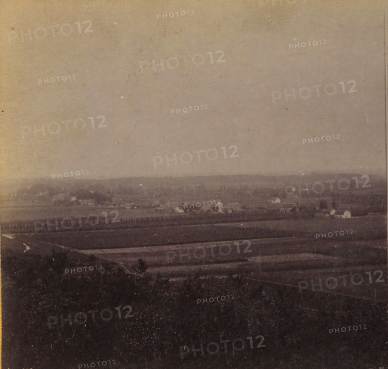 View of Leersum from the Darthuizerberg, View of Leersum, Views and landscapes in Europe, Africa and Asia, Geographical Sculpture Gallery, collected by MJ Broekhuijsen, Headmaster of a school in Amsterdam, stereograph, Numbered lower left of photo: A.18., annotation: 'taken from the Darthuizerberg (Nellenstein tomb). Arable land at the foot of the mountain.', publisher: Merkelbach & Co., Amsterdam, compiler (person in literature): Martien Johan Broekhuijsen, c. 1905, photographer, compiler (person in literature), pasteboard, paper, albumen print, height 87 mm x width 177 mm, Part of a group of 52 stereophotos used in primary education as a supplement to school charts. The entire series consisted of 274 numbers in 10 categories (A to K)., village, Leersum, A faded, grainy landscape photograph showing a wide expanse of land with layered horizontal bands of darker and lighter tones, a distant low ridge or treeline near the middle of the image, scattered small bright spots that resemble is...