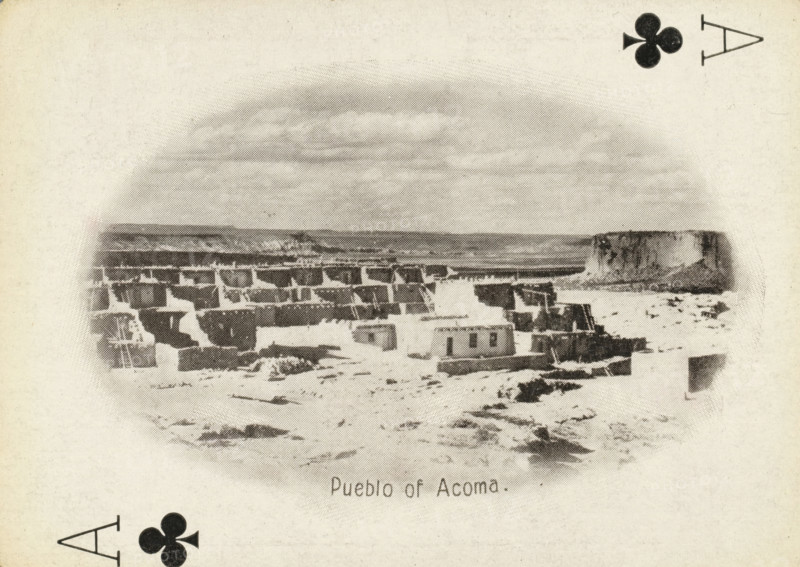 Pueblo of Acoma, Ace of clubs with a face on Acoma Pueblo, New Mexico, photograph, playing card, Playing card from a box with 53 playing cards with autotype images of Native Americans. Contents include a complete set of playing cards including joker., photographer: Adam Clark Vroman, United States of America, publisher: Lazarus & Melzer, Los Angeles (city), c. 1900, North America, paper, autotypie, height 88 mm x width 63 mm, A grainy black and white scene shows a cluster of low, rectangular adobe buildings arranged on a flat, rocky terrain with stepped terraces and flat roofs, some structures appearing partially ruined, with a wide, flat-topped mesa rising in the background and an expanse of sky above; decorative club suit symbols appear near the corners of the image.