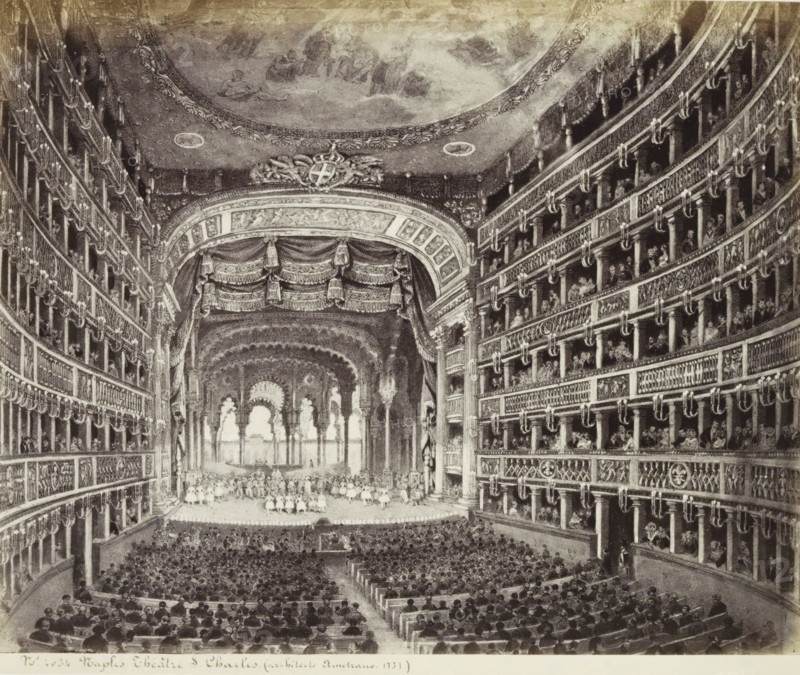 Photo reproduction of (presumably) a print of the Teatro San Carlo in Naples, Naples Theatre S. Charles. (architect Ametrano. 1737.), photograph, reproduction, Part of Travel Album with photos of sights in Naples and the surrounding area., negative number: '4034', photographer: attributed to Giorgio Sommer, after print by anonymous, c. 1865 - c. 1875, after print by, Attributed to, paper, albumen print, height 203 mm x width 244 mm, theatre (building), Naples, A wide interior view of an ornate theater with a large stage framed by heavy drapery and decorated archwork, a high curved ceiling featuring a painted dome, and multiple tiers of box seats lining both sides with detailed balustrades and decorative moldings; the stage area shows figures arranged in rows and architectural arches in the background, and the audience fills the stalls with heads seen from behind.