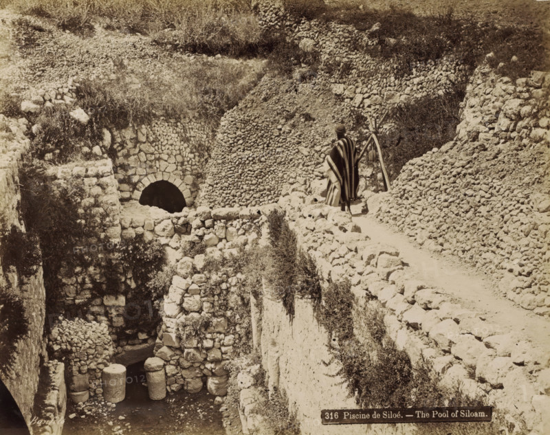 Pool of Siloam near Jerusalem, Piscine de Siloé. - The Pool of Siloam., photograph, Part of Travel Album with Photos of Jerusalem and Other Biblical Places., negative number: '316', photographer: Maison Bonfils, Jerusalem, c. 1867 - c. 1895, pasteboard, paper, albumen print, height 225 mm x width 283 mm, pond, pool, A sepia-toned scene of a rocky terrace and pathway carved into a hillside, showing rough stone walls and piled stones forming terraces and retaining structures, with an arched stone opening set into one wall above a lower chamber that contains large cylindrical stone columns partially submerged in water; vegetation and scrub grow among the stones and on the hillside, and a person wearing a striped cloak and head covering stands on the path facing away, near a simple wooden tripod or support.