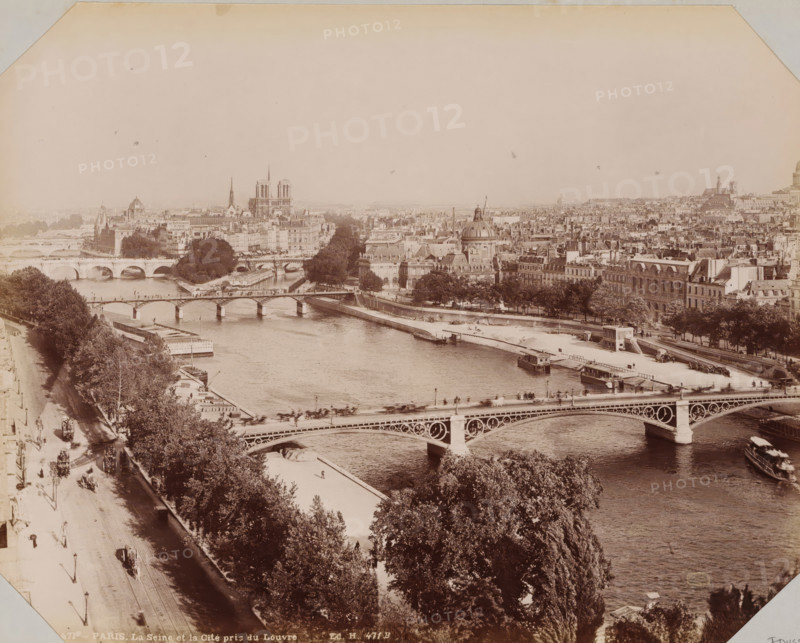 View of Paris with Notre-Dame and the Seine, album page, photograph, This photo is part of an album., inscription: '471B - Paris. La Seine et la Cité pris du Louvre. Ed. H. 471B', retailer's mark: 'E. Hautecoeur, Estampes Photographies, 35 Avenue de l'Opéra, 35, Paris', annotation: 'Travel Paris April 1898', photographer: Edouard Hautecoer (possibly), Paris, 1890 - 1898, paper, albumen print, albumendruk, height 258 mm x width 355 mm, river, church (exterior), city-view in general, 'veduta' (city(-scape) with figures, staffage), Seine, Notre-Dame (Paris), A wide sepia-toned aerial view of a city river scene with multiple arched bridges crossing the water, tree-lined embankments, riverside walkways, and boats moored along the banks; dense rows of buildings and rooftops fill the background, punctuated by domed and spired church structures, open plazas, and avenues; in the foreground a tree-covered riverside promenade runs alongside a busy street with small figures, carriages, and lamppos...