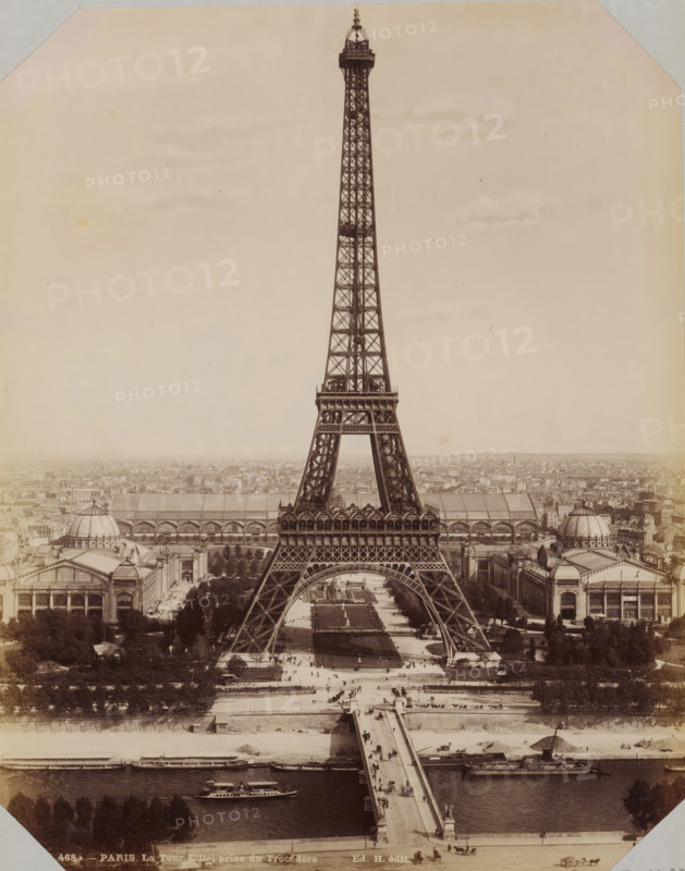 View of the Eiffel Tower, album cover, photograph, This photo is part of an album., retailer's mark: 'E. Hautecoeur, Estampes Photographies, 35 Avenue de l'Opéra, 35, Paris', inscription: '468A - Paris. La Tour Eiffel prize de Trocadéro. Ed. H. édit', photographer: Edouard Hautecoer (possibly), Paris, 1890 - 1898, paper, albumen print, height 258 mm x width 355 mm, city-view in general, 'veduta' (city(-scape) with figures, staffage), Eiffel tower, A tall iron lattice tower dominates the center of the image, rising from a wide base with four arched legs and tapering to a narrow pinnacle with an observation platform near the top; beneath the tower a broad formal garden with walkways and rectangular lawns stretches toward a bridge that crosses a river in the foreground where several boats are moored and one is underway; flanking the tower on both sides are large exhibition halls with domed roofs and arched colonnades, and rows of trees and avenues line the avenues and spaces around the bu...