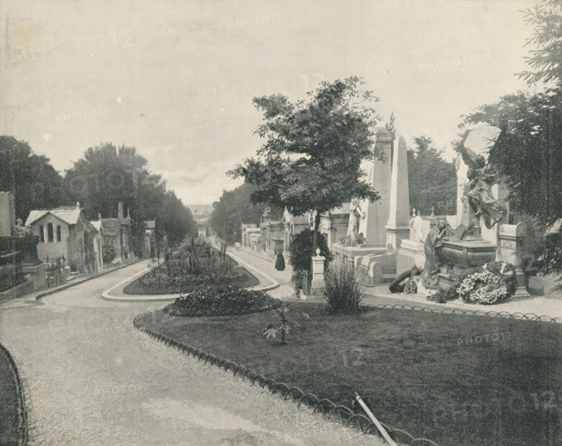 Père-Lachaise in Paris, album page, photomechanical print, This print is part of an album., maker: Angerer & Göschl, C., 1880 - 1900, paper, autotypie, height 201 mm x width 248 mm, necropolis, Paris, Cimetière du Père-Lachaise, A wide view of a tree-lined avenue with a curved pathway and a grassy central island, flanked by stone mausoleums and sculpted grave monuments, some topped with statues and ornate carvings; a few tall trees and shrubs rise among the memorials, and a person in dark clothing stands on the path near a large upright stone monument, while another sculpted figure reclines on a tomb surrounded by floral arrangements.