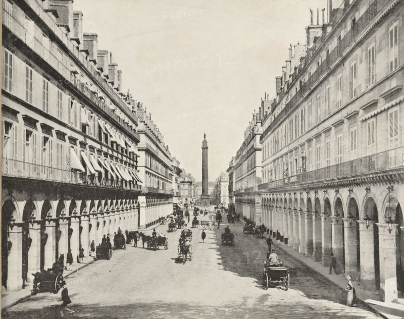 View of the Austerlitz Column, album page, photomechanical print, This print is part of an album., maker: Angerer & Göschl, C., 1880 - 1900, paper, autotype, height 249 mm x width 200 mm, historical persons, monumental adornments (in city), animal traction, animal-drawn vehicle (carriage etc.), Paris, A wide street flanked by long rows of multi-story buildings with repeating arches at ground level and shuttered windows above, a tall column topped with a statue visible in the distance at the center, horse-drawn carriages and riders moving along the street, pedestrians walking or standing near the sidewalks, decorative ironwork and awnings on some windows, and street lamps attached to the building façades.