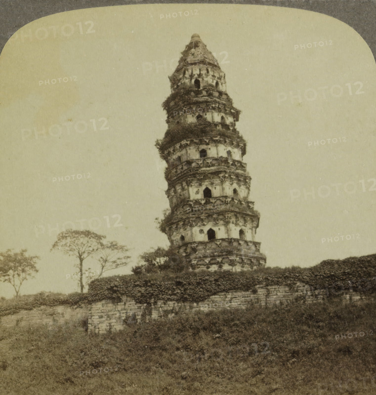 View of the Great Wall of China, Great Wall of China, stereograph, number: '95', number: '43', inscription: 'X', title: 'Great Wall of China.', publisher: Strohmeyer & Wyman, New York (city), publisher: Underwood and Underwood, 1879 - 1909, photographer, North America, pasteboard, paper, albumen print, height 88 mm x width 178 mm, city-walls, A tall, weathered multi-tiered stone tower with layered circular balconies and arched openings rises from a stone base covered in vegetation, with trees visible behind and to the side and a grassy foreground sloping down from the masonry.