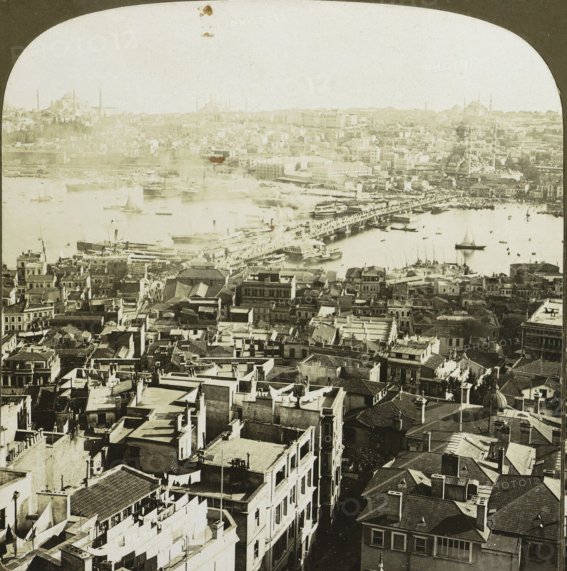 Galata Bridge over the Golden Horn in Istanbul, Constantinople, showing the Outer Bridge over the Golden Horn and Stamboul (the Turkish Quarter of the City) Turkey, stereograph, copyright notice: 'COPYRIGHT 1901 BY HC WHITE CO.', inscription: '... in, de Gouden Horn', number: '4302', inscription: 'J 3.', inscription: 'The 'PERFEC' STEREOGRAPH. (Trade Mark.), Patented April 14, 1903. Other Patents Pending.', Galatabrug, photographer: HC White Co., New York (city) (possibly), 1901, Istanbul, North America, paper, pasteboard, baryta paper, gelatin silver print, developing gelatin silver print, height 88 mm x width 177 mm, pontoon bridge, Golden Horn, Galata Bridge, A sepia-toned aerial view of a dense urban waterfront showing rows of closely packed buildings with flat and tiled roofs, narrow streets and alleys running between them, and rooftop details like chimneys, laundry lines, and small terraces; a busy harbor with various boats and sailboats scattered on the water, larger vessels doc...