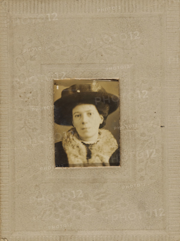 Portrait of an unknown woman with hat, quick photo, c. 1912 - c. 1918, photographer, paper, pasteboard, baryta paper, gelatin silver print, developing gelatin silver print, height 30 mm x width 22 mm, height 83 mm x width 63 mm, adult woman, anonymous historical person depicted, A sepia-toned portrait of a woman wearing a dark wide-brimmed hat with a feather and a light fur collar, mounted within a textured paper frame.
