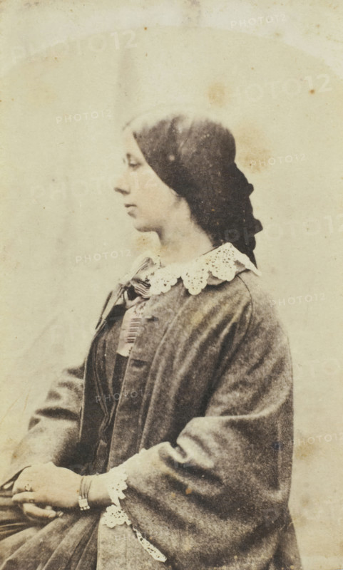 Portrait of an unknown woman, photograph, France, 1840 - 1870, photographer, paper, salted paper print, hand coloring, colored salt print, height 103 mm x width 63 mm, adult man, historical persons not known by name - BB - woman, A sepia-toned portrait of a woman shown in profile facing left, with dark hair pulled back and covered by a dark headscarf, wearing a dress with a scalloped lace collar and a cloak draped over her shoulders; her hands rest in her lap, one wrist adorned with a bracelet, and the image shows a textured, slightly stained background and aged photographic wear.