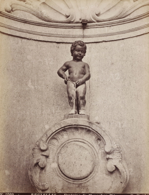 Fontaine de Manneken-Pis, Fountain of Manneken Pis in Brussels, Belgium, Bruxelles, photograph, number: 'No 1260', photographer: Gustave Hermans, Brussels, after sculpture by Jerôme Duquesnoy (II), 1884 - 1914, Jerôme Duquesnoy (II), after sculpture by, paper, albumen print, height 280 mm x width 215 mm, ornamental fountain, Manneken Pis, A stone statue of a naked child standing on a rounded pedestal, with curly hair and a neutral facial expression, positioned above an ornate carved circular relief; the child is depicted with one arm bent and the other hand touching the groin area, and a thin stream appears to flow downward from that point; the background shows a textured flat wall with horizontal molded bands and decorative scrollwork at the top and sides.
