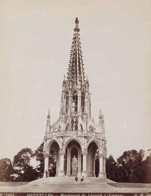 Monument to King Leopold I of Belgium in Brussels, Belgium, Monument de Léopold I (Laeken), Bruxelles, photograph, number: 'No 1265', photographer: Gustave Hermans, Laeken, 1884 - 1914, Brussels, paper, albumen print, height 281 mm x width 218 mm, Person, Leopold I (King of the Belgians), monument, statue, Monument for the Dynasty, A tall ornate Gothic spire rises from an intricately carved stone pavilion with pointed arches and clustered columns, the upper section showing delicate tracery, pinnacles, and sculptural details, while the lower section features arched openings supported by tall round columns and a standing statue on a pedestal visible within the central arch, with steps leading up to the structure and trees flanking the sides.