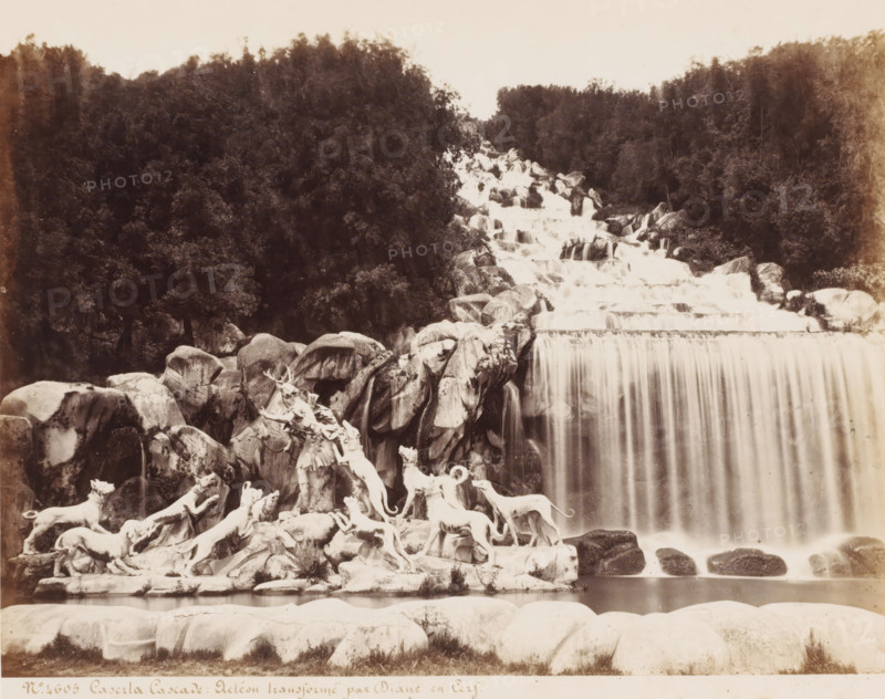 Fountain of Diana and Actaeon in the gardens of the Palace of Caserte in Naples, Italy, Caserta Acteon transforme by Diane and Cerf, photograph, number: '13', number: 'No. 4605', inscription: 'Sommer (+)', photographer: attributed to Giorgio Sommer, Naples, after sculpture by various manufacturers, 1857 - 1914, various manufacturers, after sculpture by, Attributed to, pasteboard, paper, albumen print, albumendruk, height 307 mm x width 403 mm, ornamental fountain, Actaeon changed into a stag: as punishment for seeing her bathe, Diana changes Actaeon, the hunter, into a stag (Ovid, Metamorphoses III 193), Caserta, Palace of Caserta, A wide cascading waterfall flows over stepped rock ledges with water streaming in vertical sheets into a pool below, framed by a dense dark forest on either side; in the foreground a rocky outcrop holds a group of pale sculpted figures and animals, including standing and leaping dogs and a central human figure reaching upward toward a stag-like creature, all...